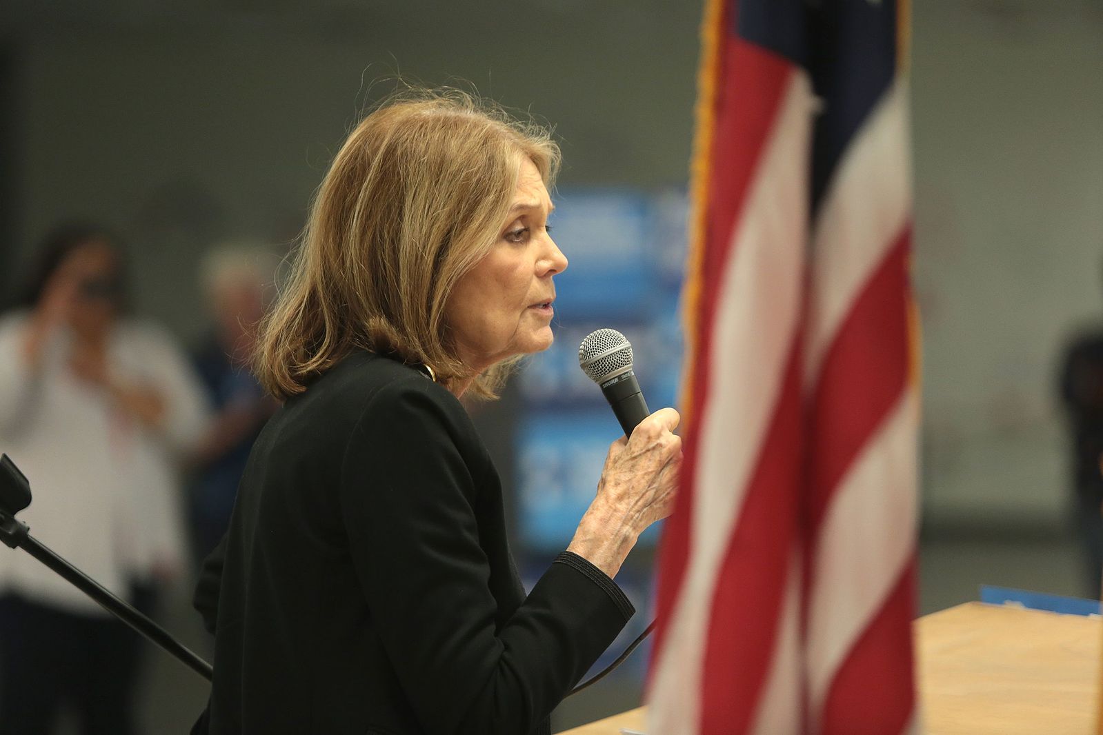 Gloria Steinem speaking in front of an American flag