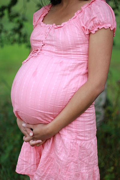 A pregnant woman in a pink dress holds her stomach. 