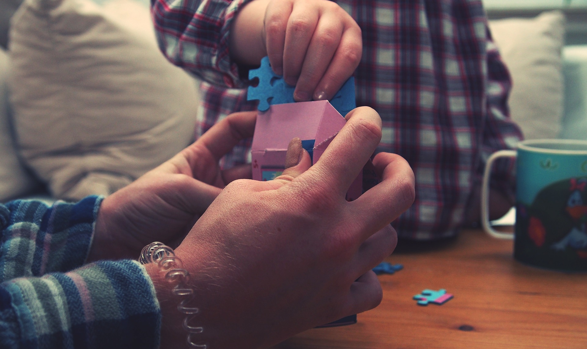 An adult hands open a tiny pink box, as a child hand holds two puzzle pieces.