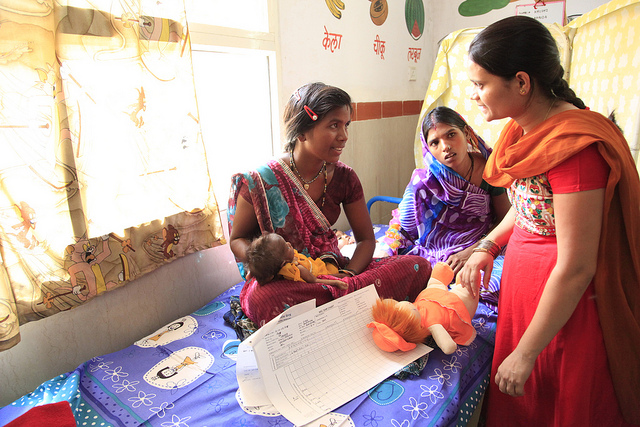 Indian woman sitting on bed holding a baby surrounded by two other Indian women 