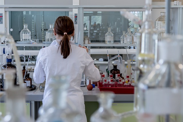A woman scientist is turned away from the camera, and faces a laboratory desk filled with equipment. 