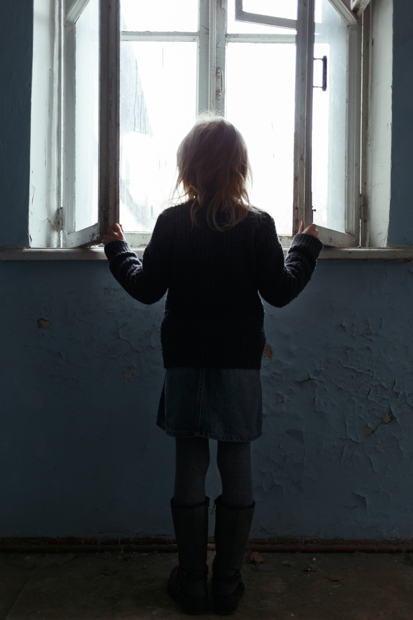 young girl stands in front of a window with back to camera