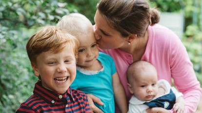 Mother with three children--kissing one on the cheek and holding one