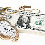 A bent golden pocket watch rests on a stack of US dollar bills.