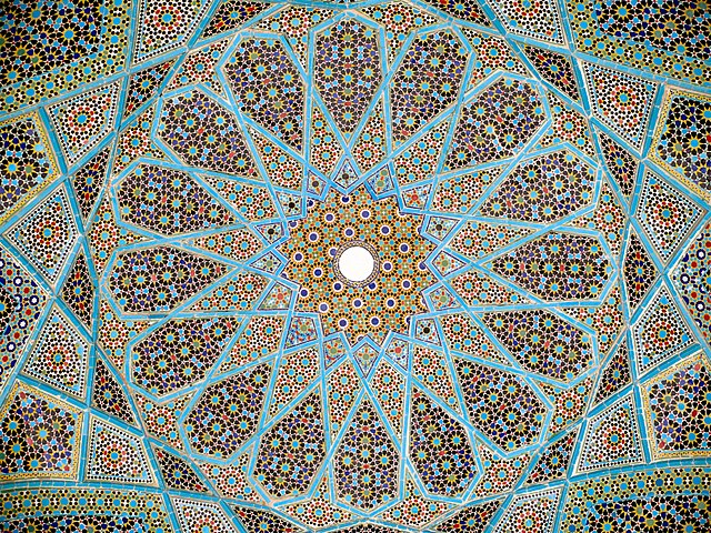 A mosaic made of primarily blue, black, and green tiles forms a radial pattern around a central circle.