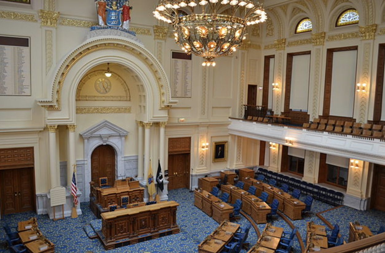 Interior image of New Jersey state house showing rows of chairs, a chandelier, etc.
