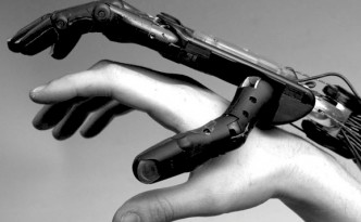 A black and white image of a robotic hand lightly grasping a human hand.