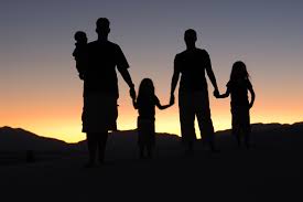 A shadow of a family of 5 holding hands in front of a sunset. Two parents, two toddlers, and a baby.