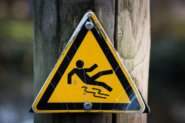 A triangular warning sign posted against a wooden post. The sign is yellow, with a figurine that is slipping on water.