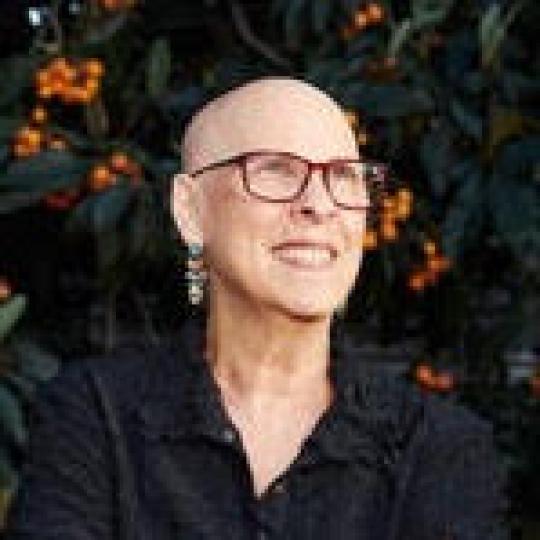 a white, bald woman smiles with glasses