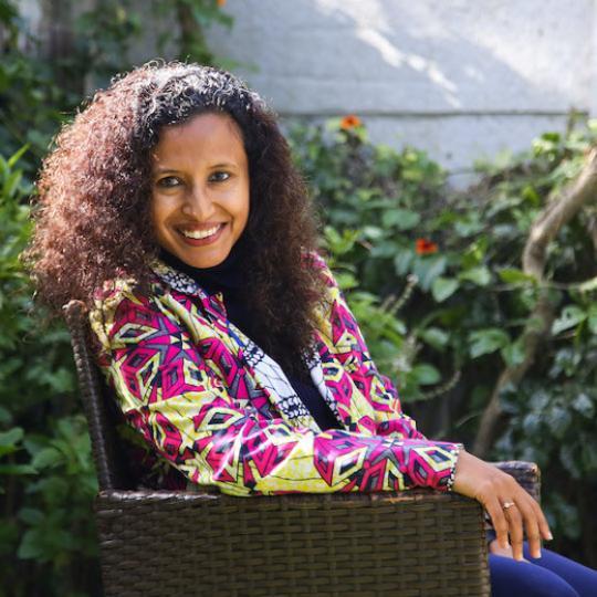 a picture of a woman with curly brown hair and a patterned jacket 