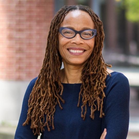 a Black woman with dreadlocks and glasses smiles