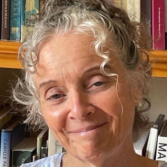 a woman with grey hair smiles in front of a bookshelf