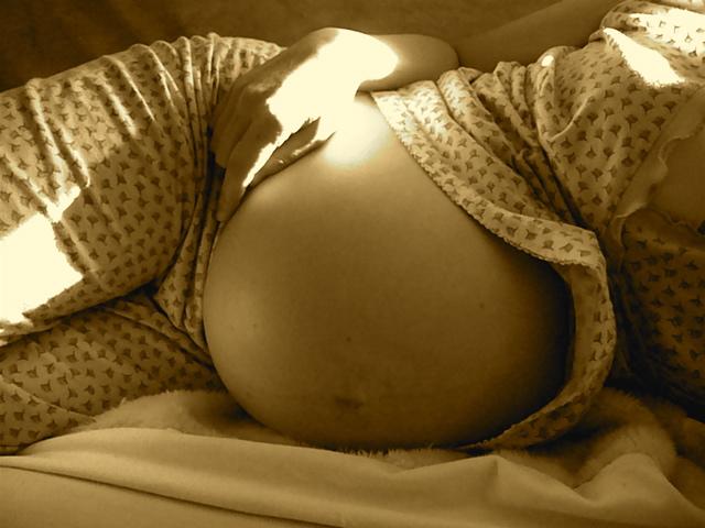 The belly of a pregnant woman lying down is featured. The photo is filtered in sepia tone.
