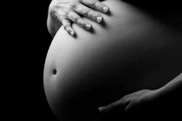 Black and white photo of a pregnant woman's belly, with her right hand placed on top of her stomach.