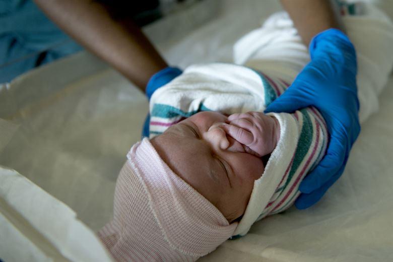 Image of a newborn baby being handled by a nurse.