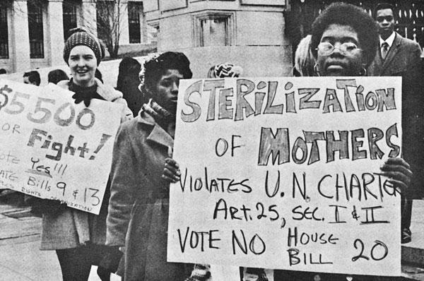 a woman holds up a sign protesting sterilization of women
