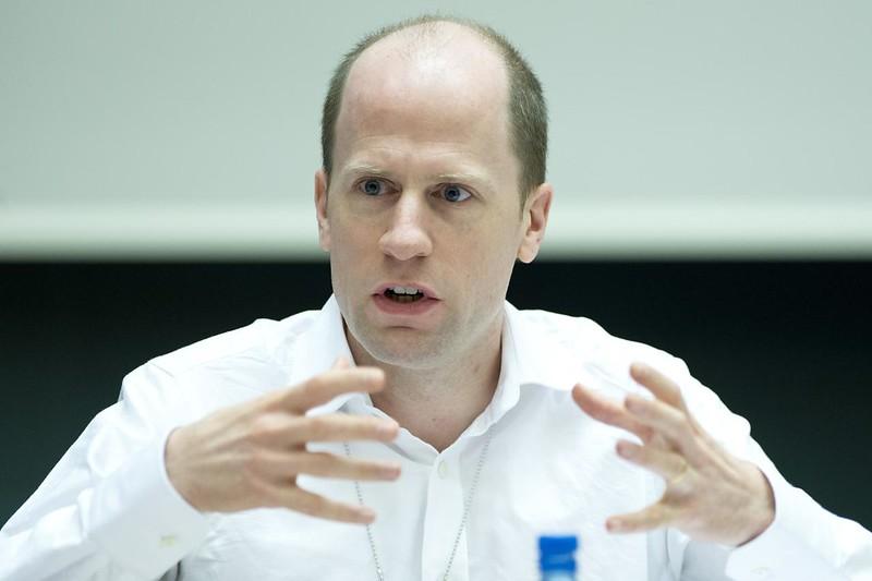 Nick Bostrom talking with a white button up. His hands are gesturing in front of him.