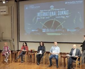 Five speakers seated on a stage in front of a logo for the International Summit