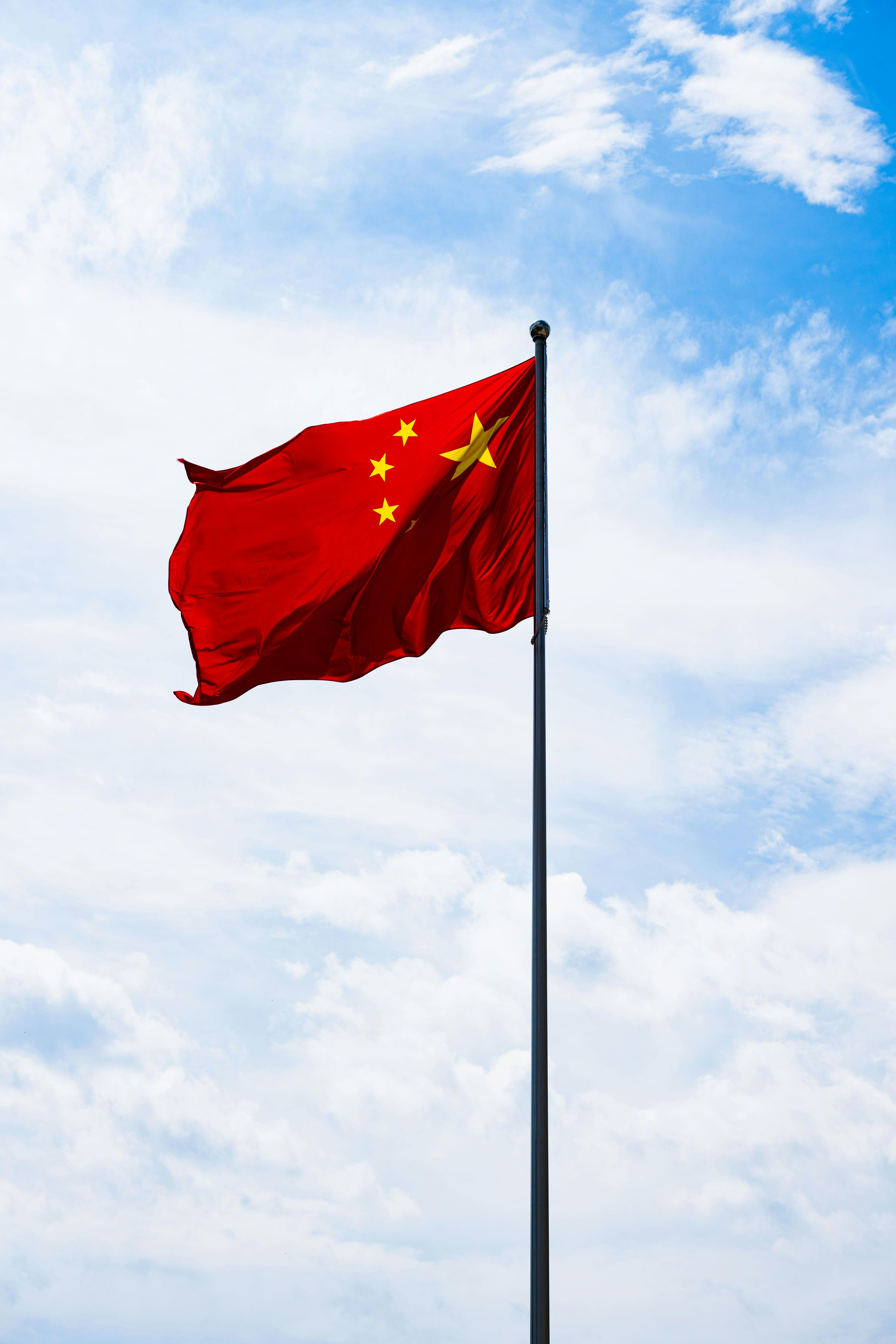 Chinese flag on flagpole with blue sky and clouds in background
