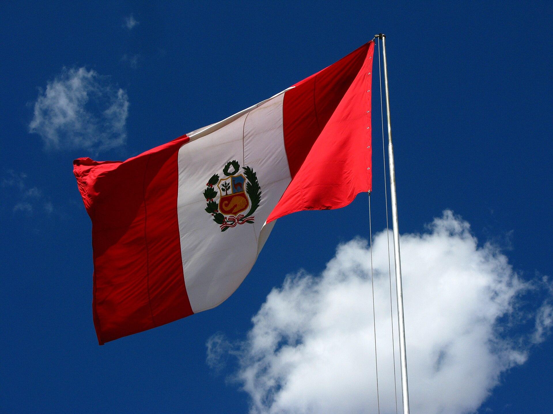 flag of Peru on flagpole with blue sky and clouds in the background