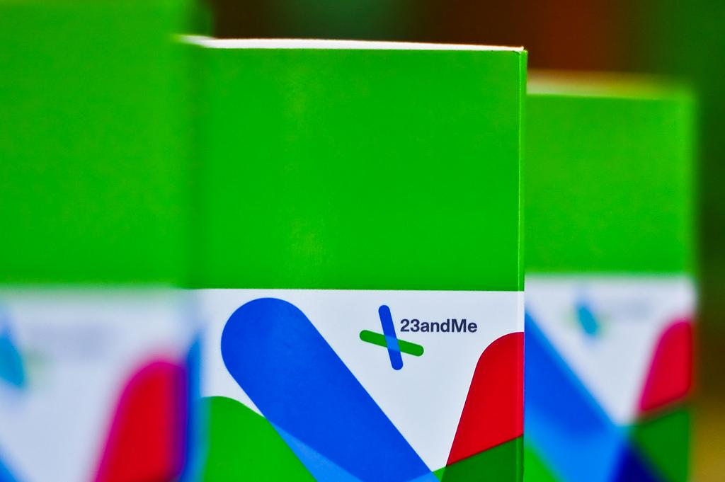 Three boxes of 23andMe kits stand upright in a line. Two of the boxes have been blurred, and one of them is centrally focused.