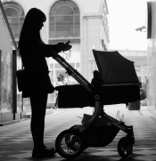 Black and white image of woman's silhouette looking at her phone while pushing baby carriage in a European city