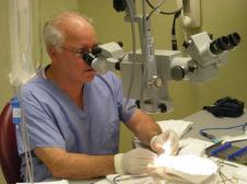 A man dressed in scrubs peers into a large microscope-like device and examines a specimen.