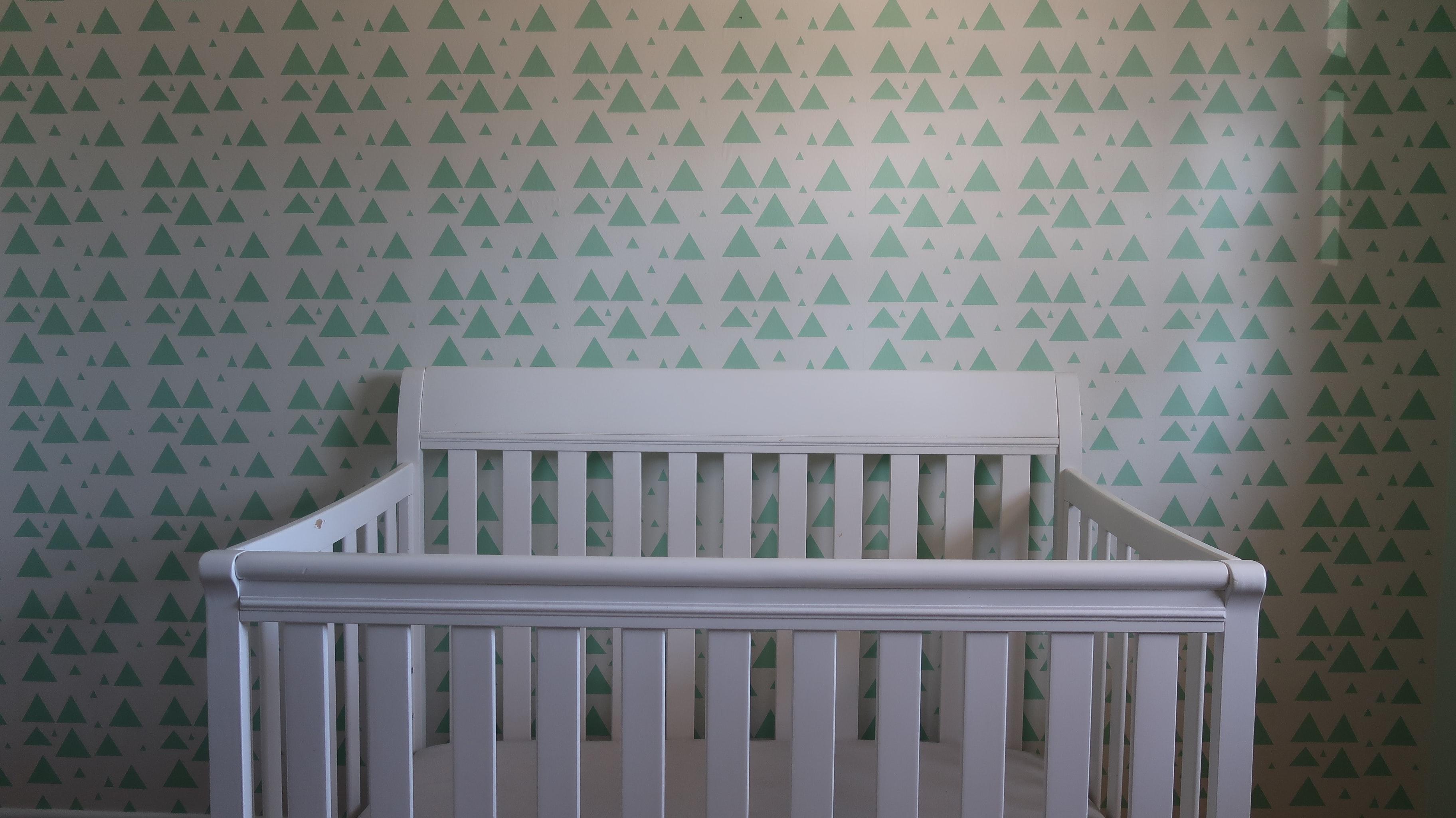 An empty white crib against a mint colored wall.