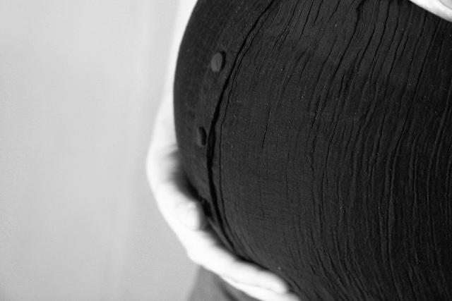 Close up of a pregnant belly covered by a t-shirt. A hand gently rests caressing its side. The picture is filtered with gray scale.