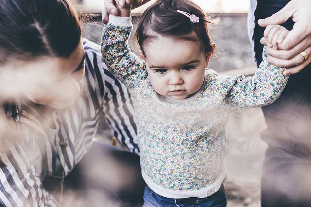 A little girl holds adults hands as they balance walking.