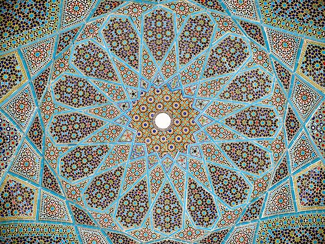 A mosaic made of primarily blue, black, and green tiles forms a radial pattern around a central circle.