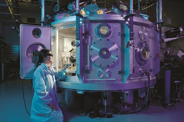 A person dressed in a lba coat looks through a large chamber 