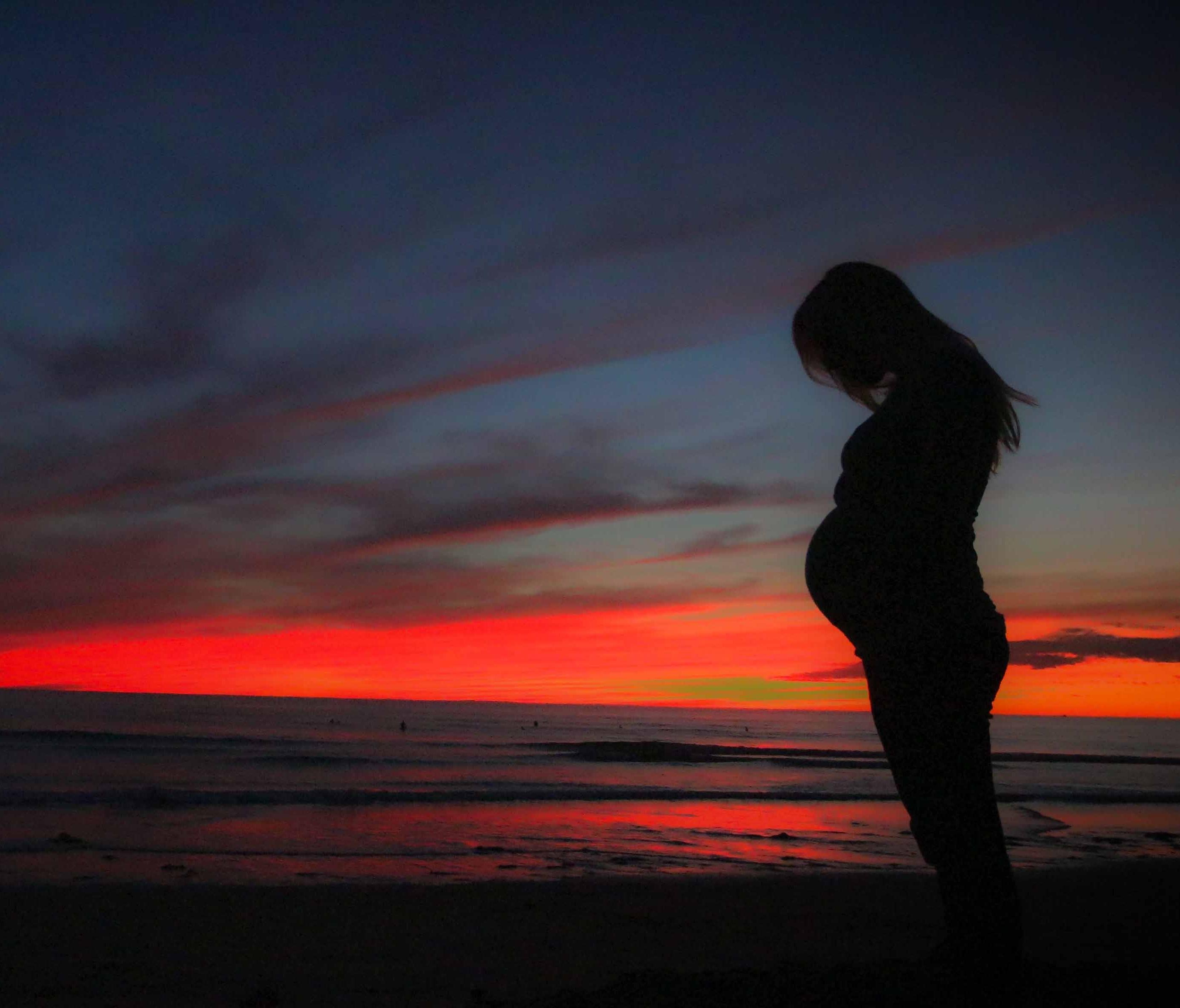 Black silhouette of pregnant woman against vibrant orange and red sunset