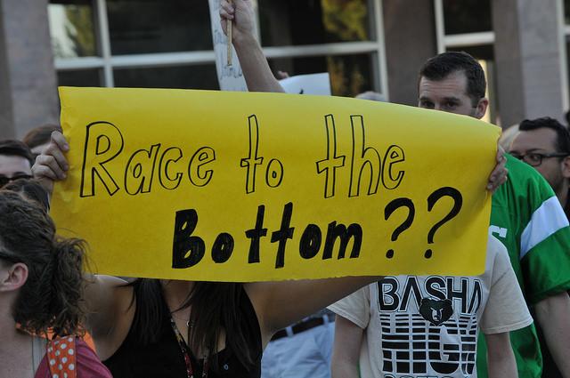 Protesters hold a yellow sign that reads, "race to the bottom??"