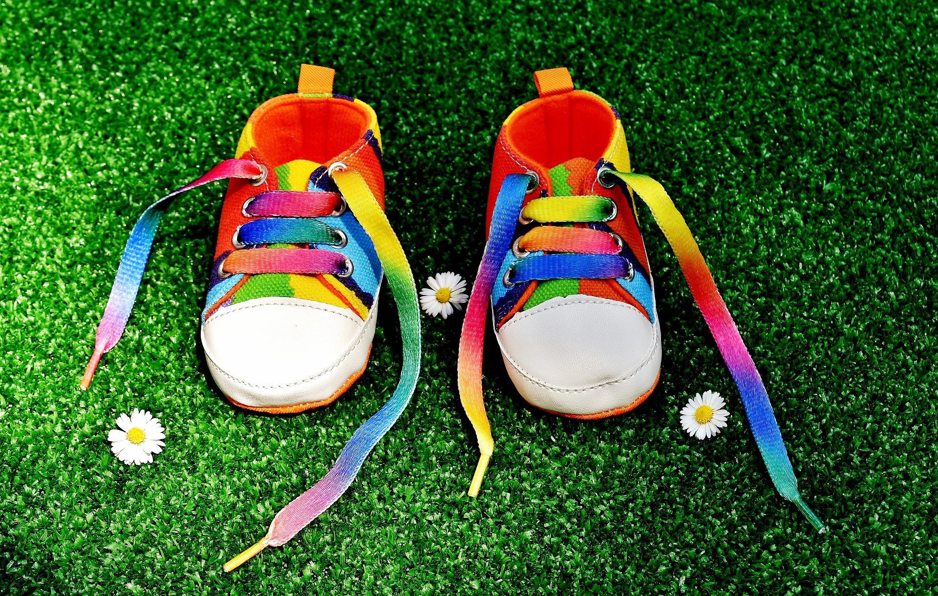Rainbow colored baby shoes on bright green grass with a few daisies