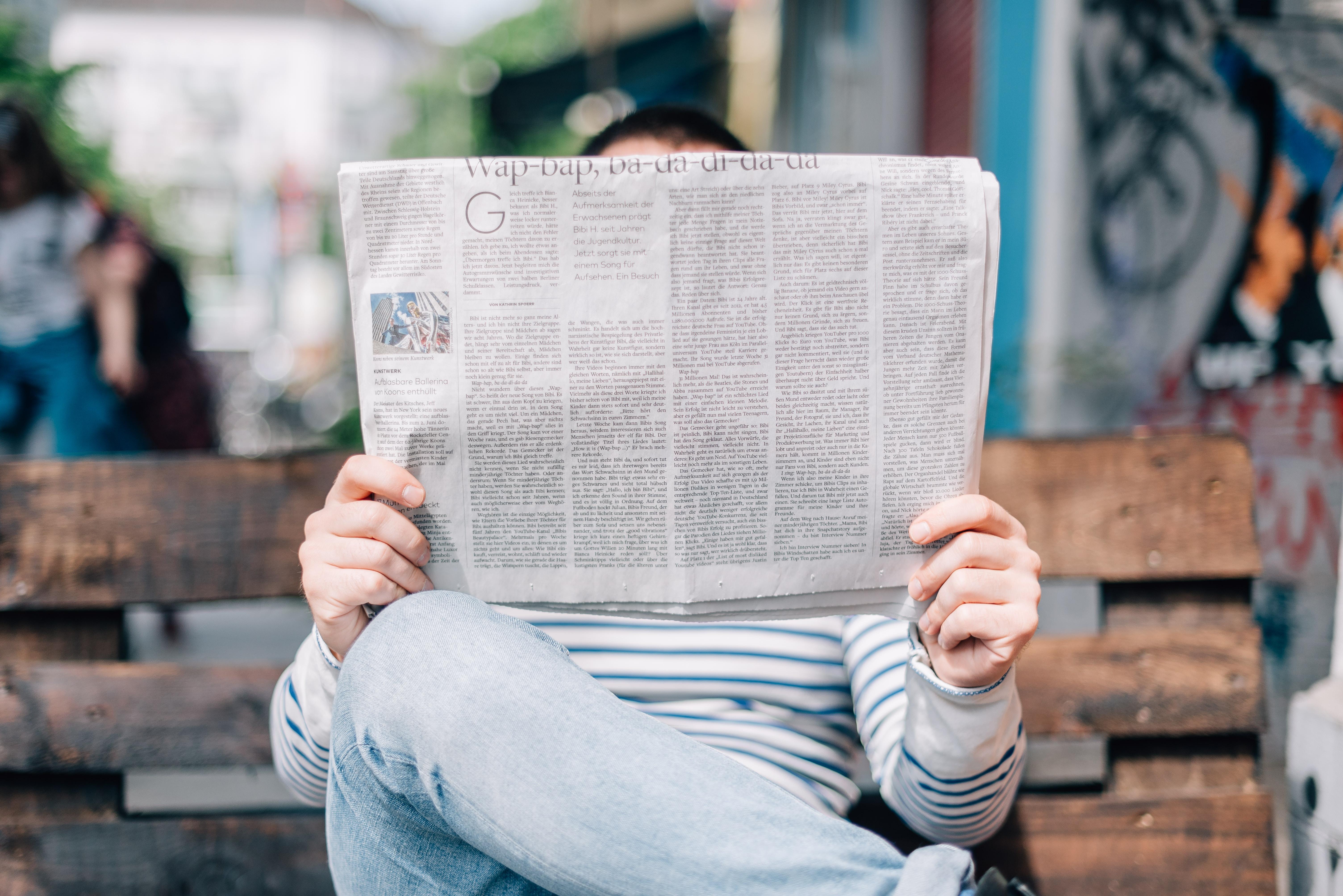 Person holding up newspaper in front of their face