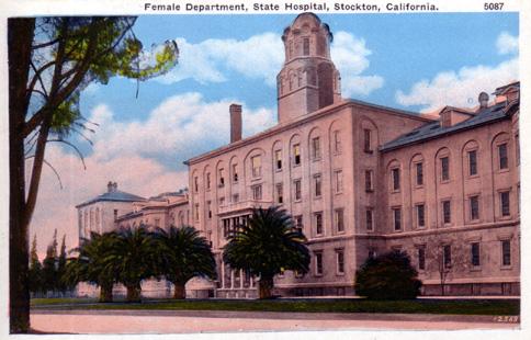 Postcard from around 1910 with the title "Female Department, State Hospital, Stockton, California." Shows the front of a large pinkish building, four stories tall in the center with a tower, and two wings with three stories each. There are a few small palm trees and other trees in front of the building.