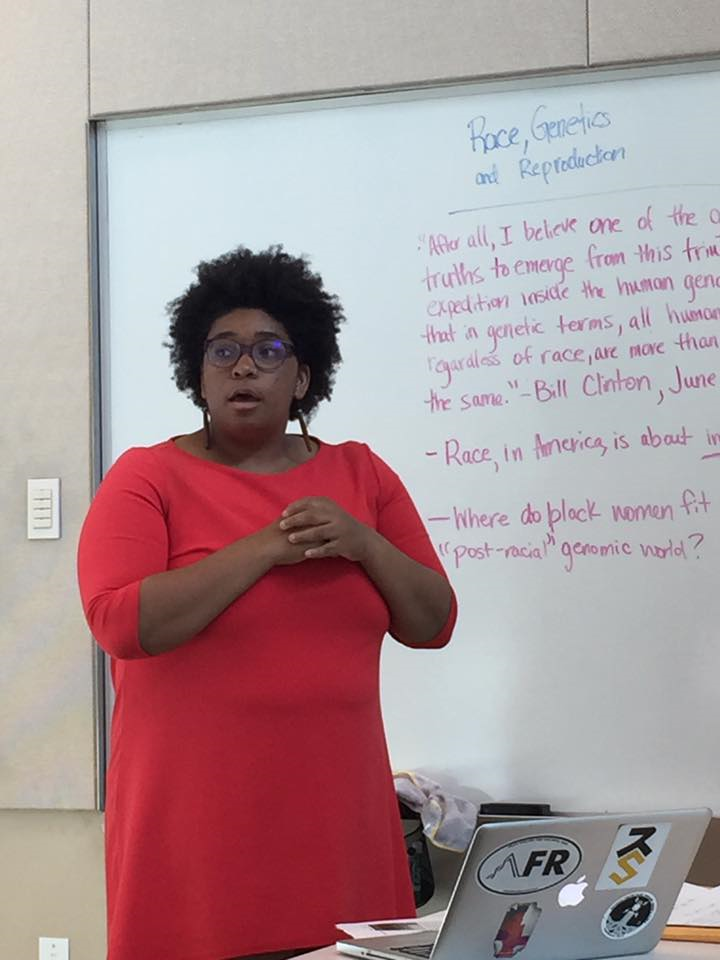 Photo of Victoria during the workshop, with a board that reads "Race, Genetics, and Reproduction."