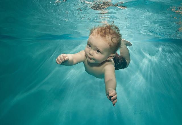 A white baby is swimming under water, with arms reaching out.