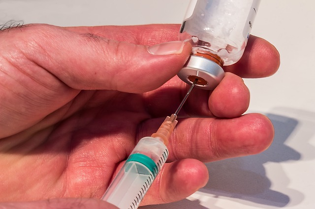 An individual uses a sringe to extract fluid from a medical vial. 