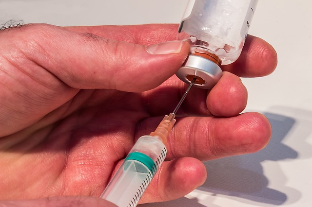 An individual uses a sringe to extract fluid from a medical vial.