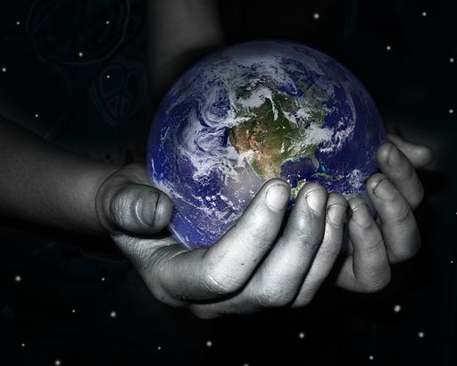 A grayscale image of a person's hand is shown, as it gently holds a colorful image of earth in their hands.