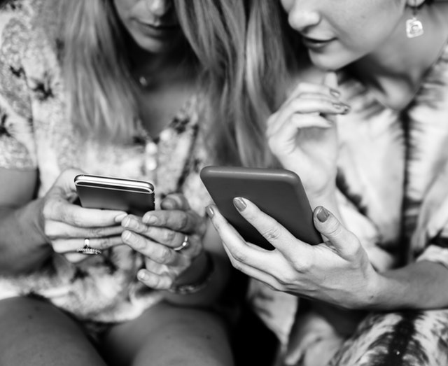 Grayscale photo of two women who are sitting next to each other, looking at each other's smartphones.