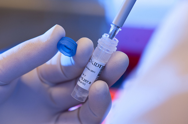 Close up of a hand holding a test tube and inserting a pipette into the tube.