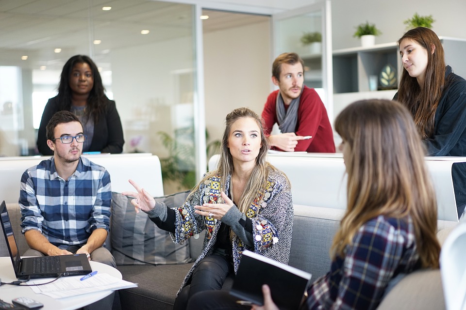 5 Individuals are sitting around a white coach work space all engaging in conversation. 